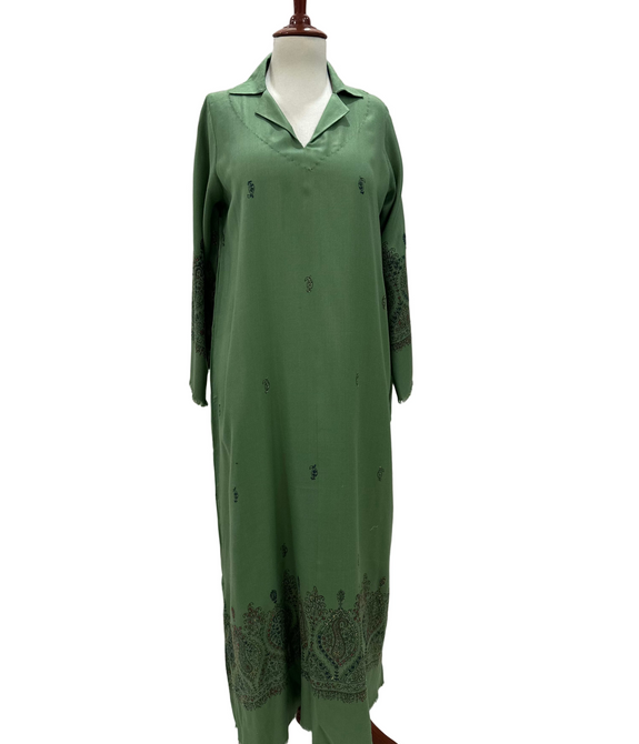 Green dress on a mannequin against a white paneled wall.